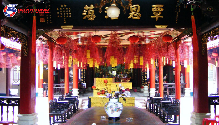Interior of a temple in Hoi An with red columns, lanterns, and incense coils hanging from the ceiling