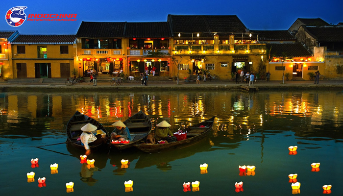 Lantern-lit boats on the river in Hoi An Ancient Town at night, with illuminated yellow buildings in the background