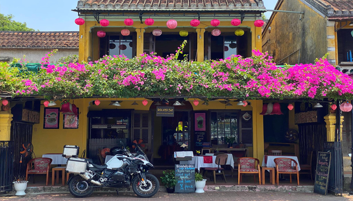 Front view of a café in Hoi An with pink bougainvillea flowers and a motorcycle parked outside.