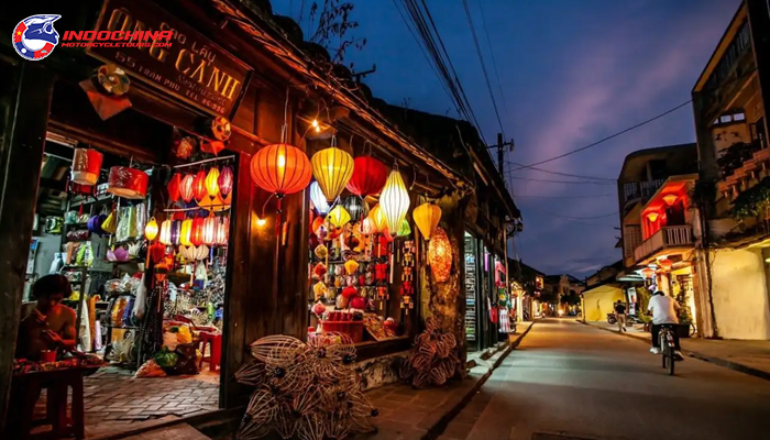 Street in Hoi An at dusk with colorful lantern shops and a cyclist passing by.